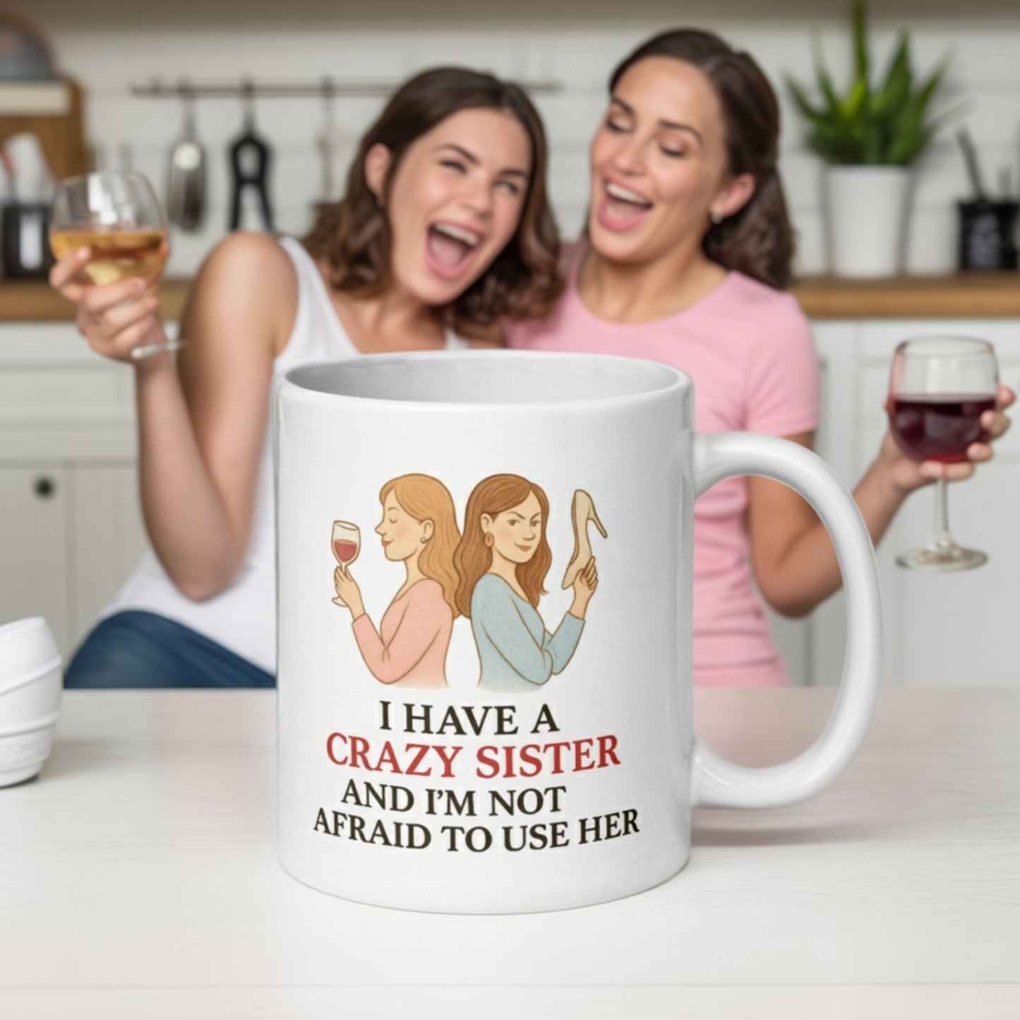 Two women laughing and holding wine glasses in a kitchen, with a mug in the foreground that reads “I have a crazy sister and I’m not afraid to use her.” One woman holds a high heel, matching the playful energy of the mug’s design.