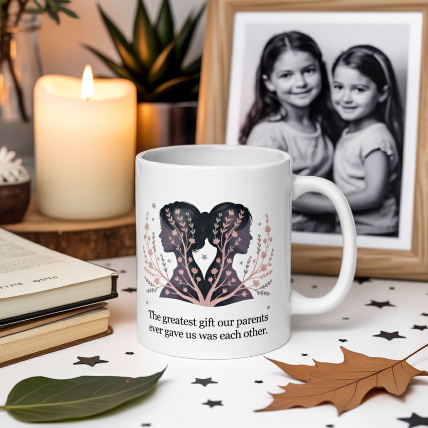 Sentimental sister gift mug on a cozy table with fall leaves, a candle, and a childhood photo of two sisters in the background. Mug reads: 'The greatest gift our parents ever gave us was each other.'
