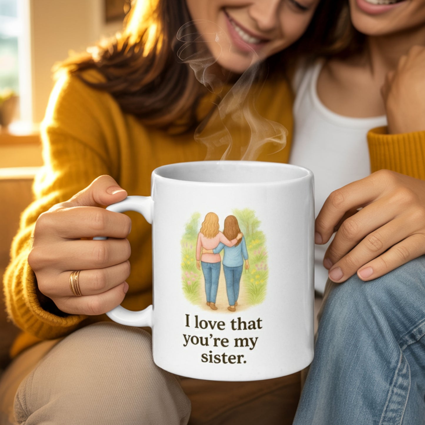 Two smiling women sit close together on a cozy couch, holding a steaming white mug that reads "I love that you’re my sister," with an illustration of two women walking arm-in-arm through a garden path.