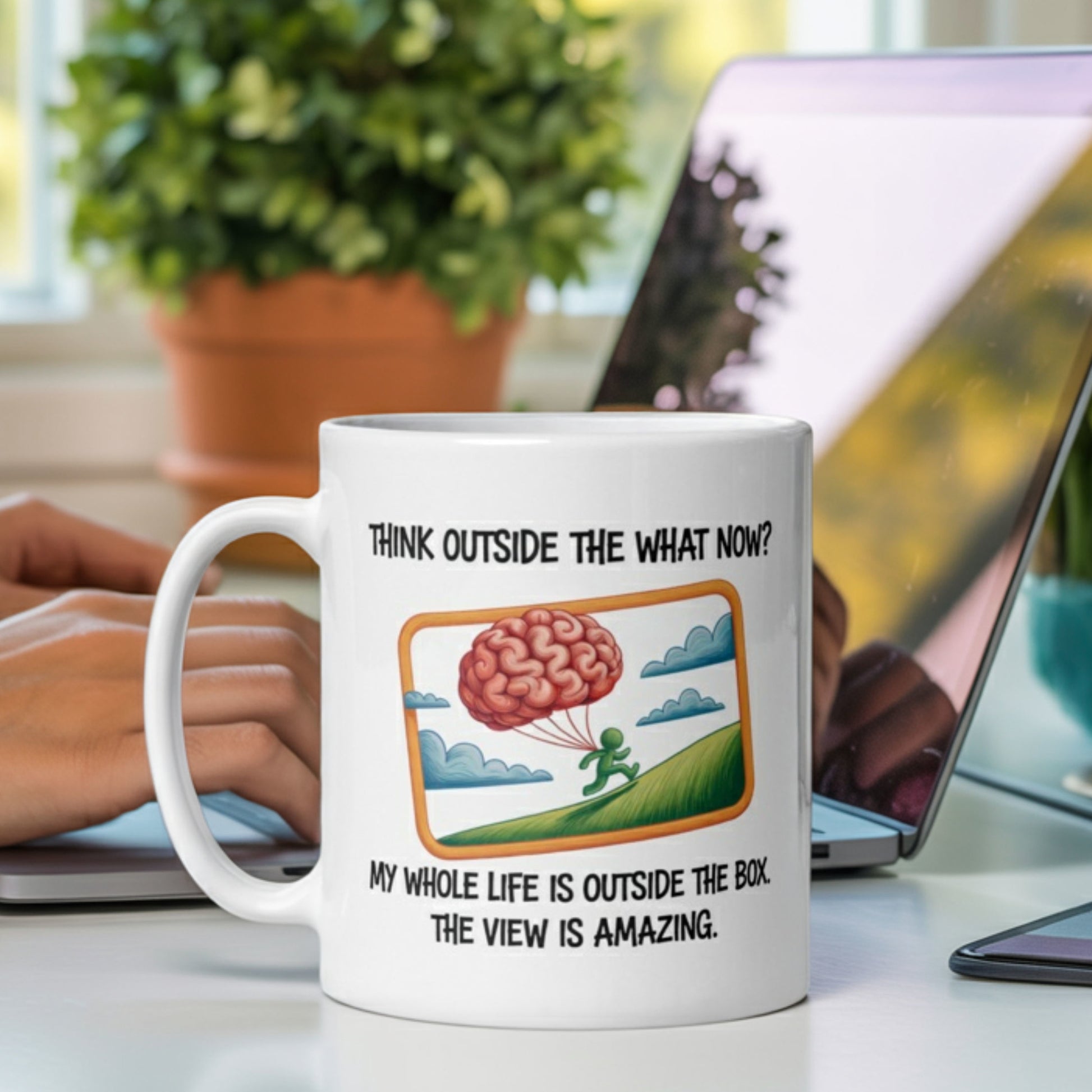 Funny white ceramic desk mug with a brain-parachute cartoon and the caption: “Think outside the what now? My whole life is outside the box. The view is amazing.” Perfect for neurodivergent thinkers, introverts with a rebellious streak, and lovers of sarcastic office humor. The mug sits on a modern desk beside a laptop, ideal for remote workers, creatives, and anyone embracing their weird, wired brilliance.