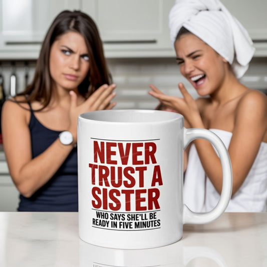White ceramic mug printed with the phrase "Never trust a sister who says she'll be ready in five minutes" in bold red and black lettering, placed on a kitchen counter. In the background, one woman in a towel is laughing while the other glares with crossed arms, capturing a playful sibling argument.