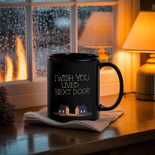 Black ceramic mug with the message "I Wish You Lived Next Door" in starry text, sitting on a cozy wooden windowsill with a knit coaster, warm indoor lighting, and raindrops on the window—perfect long-distance friendship gift for best friends, sisters, or long-distance relationships.